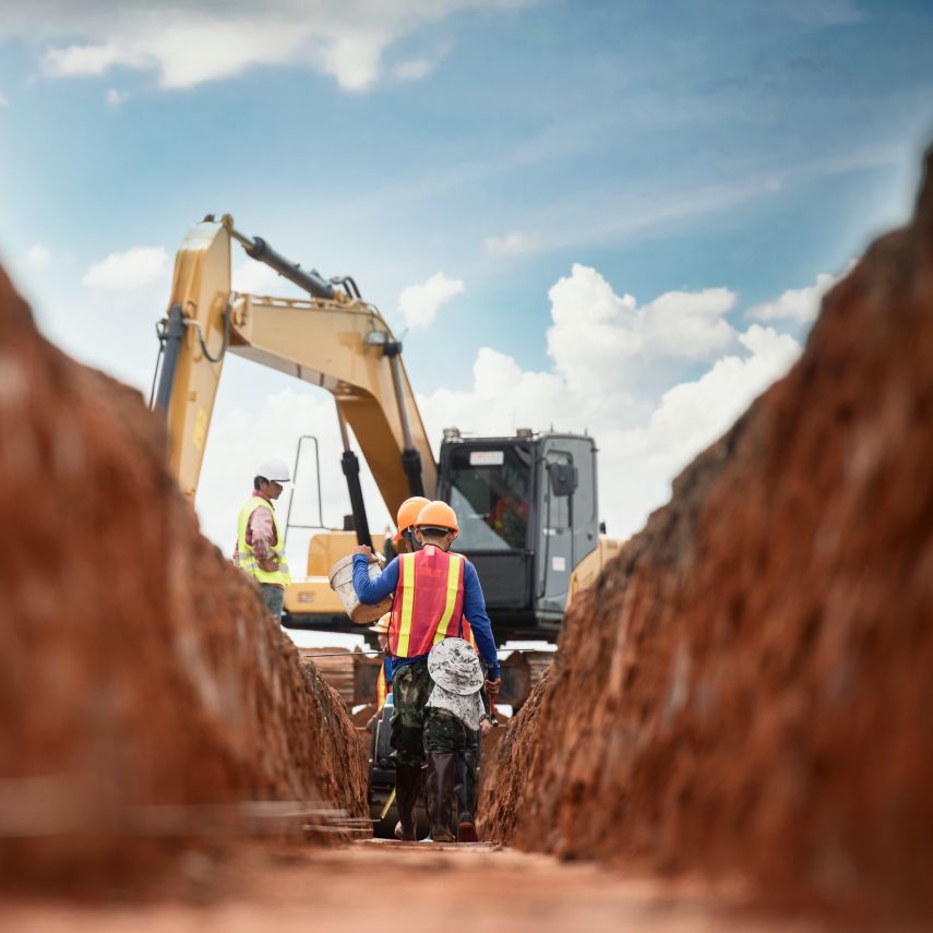 Bagger mit Mitarbeitern im ausgehobenen Graben
